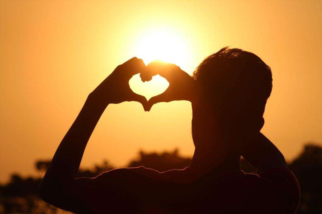 Silhouette of a man forming a heart with his hands against the sun